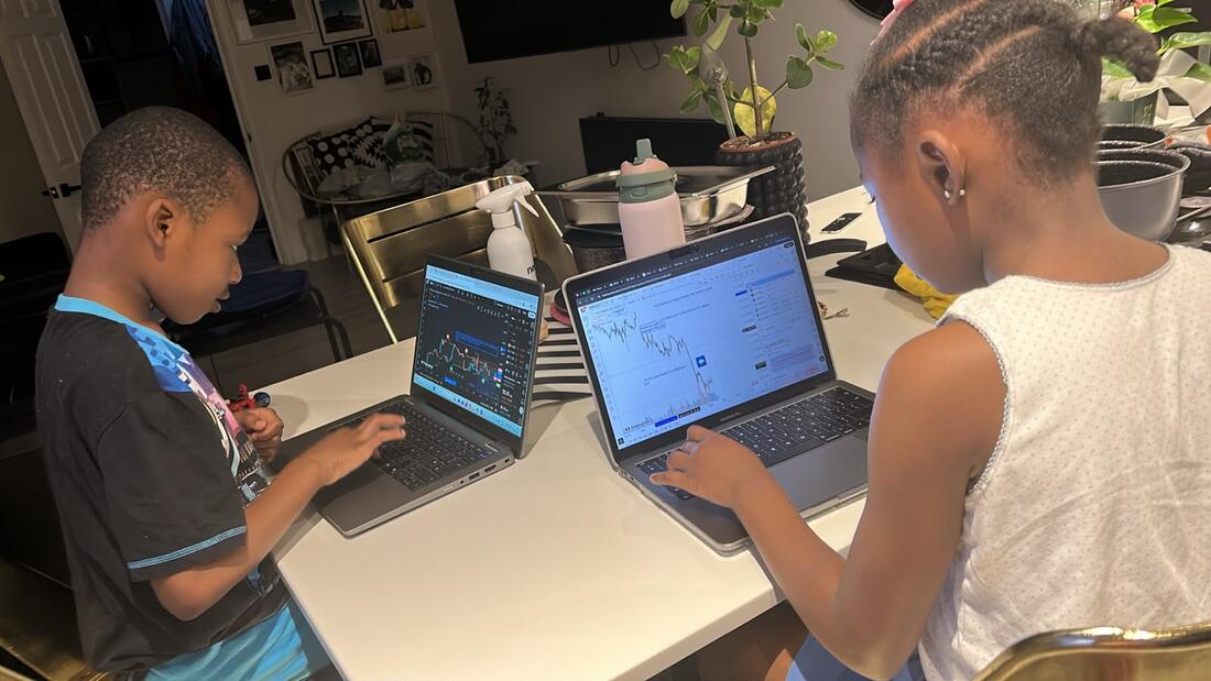 Two young learners at a kitchen table completing a home mission on their laptops